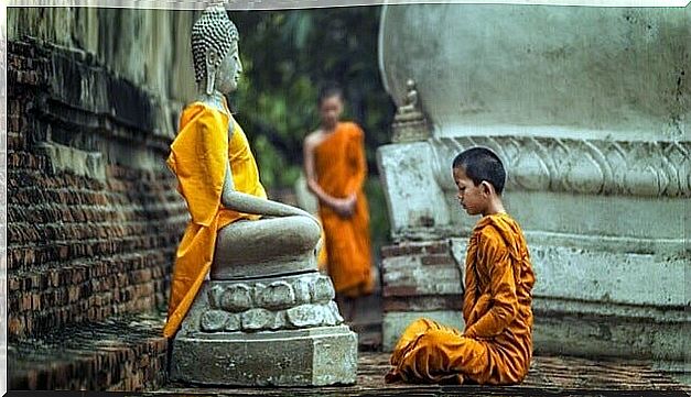 Buddhist monk meditating near a statue of Buddha